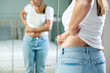 © dragonstock - Young woman touching her belly looking in mirror at home