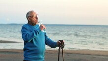 Elderly Man Scandinavian Walking Stick Relaxing Drinking Water At Sea Sand Beach Contemplate Sunset