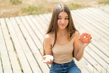 Poster - Teenager girl holding a donut at outdoors making doubts gesture while lifting the shoulders