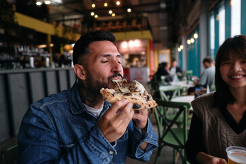 Latin man enjoying his moment eating a piece of pizza