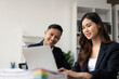 © ArLawKa - Two Asian business men and women smiling happily working with laptops and financial documents. They talk about their projects and brainstorm creative ideas together in the office.
