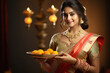 © PRASANNAPIX - Indian woman holding sweet meal or laddoo thali. Celebrating diwali festival.