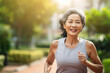 © pangamedia - A beautiful strong Asian woman is running concentrated and smiling in a beautiful city park ; a fit senior person