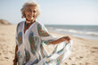 A senior old beautiful latin woman is walking on the sand next to the waterline with a dress on an European beach with a calm ocean - spring weather beach relaxing