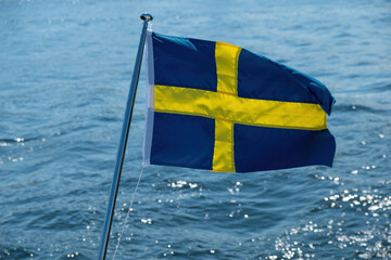 Sticker - Sweden national flag waving on boat flagpole, blur sea water background,