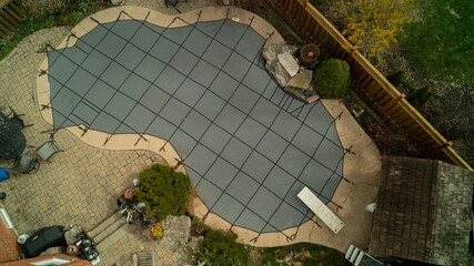 An aerial view of a safety cover over a swimming pool in the backyard on a spring day