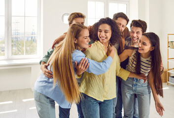 Wall Mural - Group of a happy smiling young people students having fun standing at home, hugging at meet indoors and enjoying spending time together. Friendship, party and friends meeting concept.