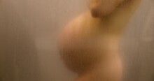 Pregnant Woman In Shower Showing Belly Bump Naked Out Of Focus Blurred Beautiful Body During Pregnancy 3rd Trimester. Maternity Photo In Steam Bath Shower. Expectant Woman Using Healthy Products.