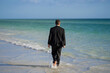 Rear view of back business man in suit in sea water at beach. Crazy business vacation. Funny businessman with laptop in formal wear near tropical beach. Hot business summer.