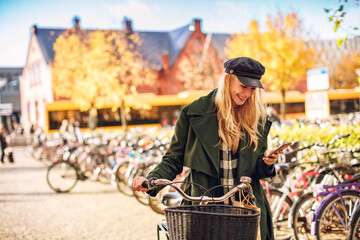 Wall Mural - Young woman using a smartphone while pushing her bicycle in the city