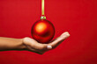 © ADDICTIVE STOCK - A hand holding a red ornament on a red background created with Generative AI technology