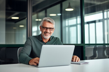 Content Older Business Professional, Grinning as He Tackles Tasks on His Laptop, Working Comfortably from His Desk