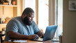 © MVProductions - Portrait of an overweight African American man working from home on a laptop computer