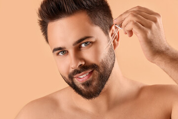 Poster - Handsome man applying cosmetic serum onto face on beige background, closeup