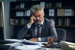 © Ivan - Desperate or sad middle aged businessman sitting pensively behind his desk in the office with a lot of documents on the desk.generative ai