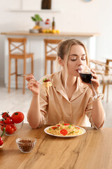 Wall Mural - Young woman with tasty pasta drinking wine in kitchen