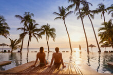 Couple On The Beach At Sunset, Honeymoon Travel, Man And Woman Sitting Near Swimming Pool In Hotel Resort