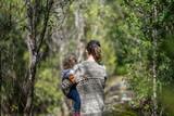 Fototapeta  - Mother with baby in a carrier on her chest on a hike, taking a bush walk in Summer in a national park in Sydney, nsw, Australia