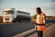 Leinwandbild Motiv In orange colored uniform, with tablet. Black man is standing on the road with truck on it