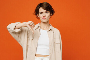 Wall Mural - Young sad disappointed displeased caucasian woman she wearing beige shirt casual clothes showing thumb down dislike gesture isolated on plain orange red background studio portrait. Lifestyle concept.