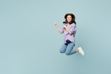 Wall Mural - Full body young happy woman she wearing purple shirt yellow t-shirt casual clothes jump high point index finger aside on area isolated on plain pastel light blue background studio. Lifestyle concept.