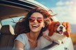 Happy young woman with cute dog driving a car on the way at sunset, travel concept.