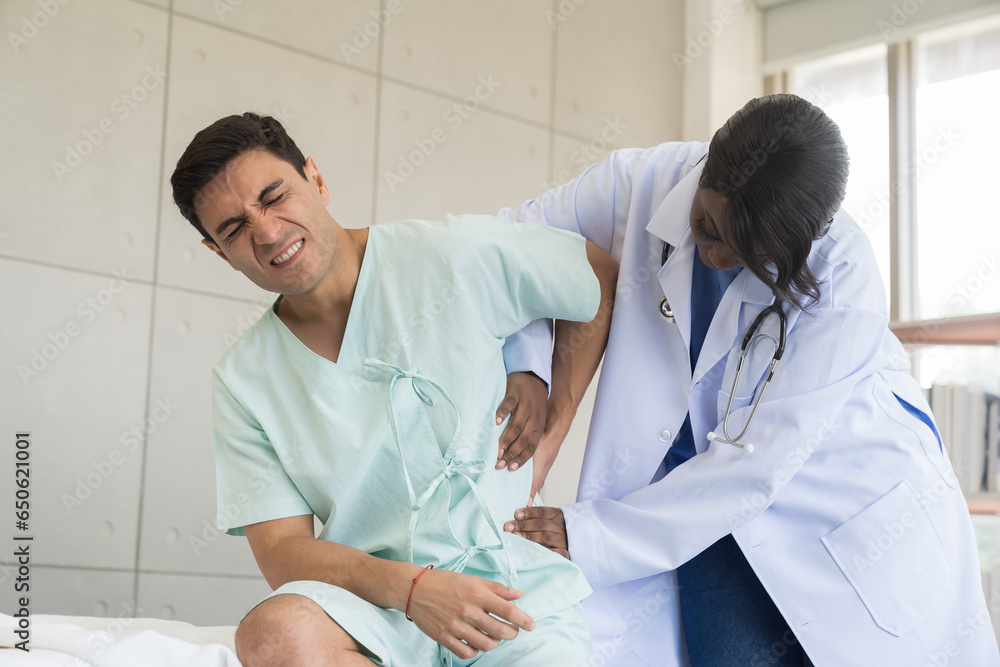 Female nurse caring male patient with careful on bed at hospital. Female assistant taking care male patient feeling back pain at clinic