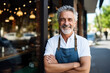© wolfhound911 - Happy middle aged older adult man small local business owner standing outside own restaurant.