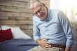 An elderly man holds his stomach in pain.