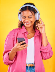 Wall Mural - Headphones, cellphone and young woman in a studio listening to music, playlist or radio and networking. Happy, phone and female model from Mexico streaming a song or album by yellow background.