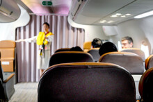 Seats In Cabin Airplane With Blurred Background Of Cabin Crew Air Hostess Show Safety Rules Before Fly, Flight Attendant Stand Aisle Inside Aircraft To Train Safety Measures Instruction To Passenger.