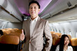 Portrait of Asian senior businessman giving arms crossed, standing on aisle inside airplane, male passenger in suit on business trip in aircraft, businesspeople traveling with airline transportation.