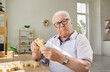 © Studio Romantic - Demented senior man playing with jigsaw puzzle. Old man with Alzheimer's disease sitting at desk in geriatric clinic or nursing home, holding wooden puzzle piece, looking at camera. Dementia concept
