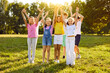 © Studio Romantic - Happy kids having fun outdoors in the summer. Group of children playing in a green park. Several joyful little friends standing on a green lawn, smiling and raising their hands up