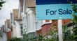FOR SALE' estate agency sign on street of typical British terraced houses