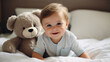 Toddler smiling while sitting on bed with a toy. Portrait of a happy and cheerful baby