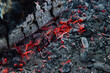 Close up of red embers in pit of ashes with chunk of black log and cracked surface