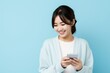 © Tuyres - Cute Japenese Fictional Woman Using Phone and Smiling. Isolated on a Plain Light Blue Background. Generative AI.