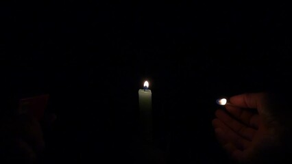 Wall Mural - person lighting a candle with a match isolated on the empty black background