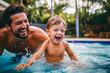 Father in a swimming pool with his young toddler son. Moment of joy, laughter, and candid moments, celebrating summer and happy parenthood