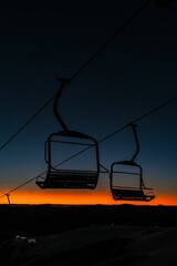 Poster - two ski lifts on a snowy hill near mountains at sunset