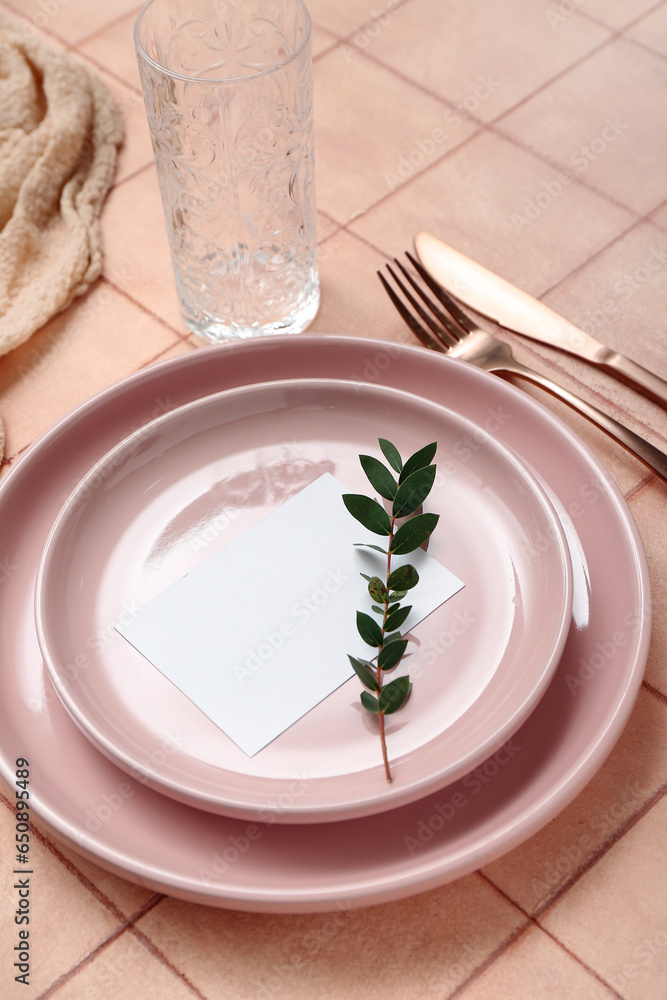 Plates with cutlery, blank card and glass on pink tile background