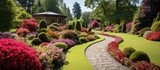 Fototapeta Londyn - Vivid flowerbeds and curving grass pathway in charming English garden