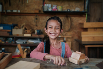 A 7 years old asian little girl is learning to make diy wooden toys in wood workshop. Concept of kid hand made education, homeschool, montessori.