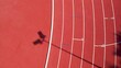 Top-down aerial view of a lamppost's shadow cast on the track at an athletics stadium.