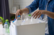 Woman sorting recycled plastic bottles into trash can at home