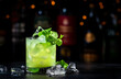Green Negroni cocktail drink with dry gin, aperitif, gentian liqueur, fresh mint and ice. Black bar counter background, bar tools, bottles