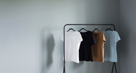 Sticker - T-shirts of neutral colors on  black hanger against  gray wall