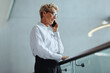 © Jacob Lund - Professional woman talking on the phone as she stands on a balcony in an office