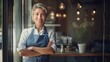 © Suleyman - Happy woman standing in front of store door in a portrait. A cheerful older waitress welcomes customers at the coffee shop.
